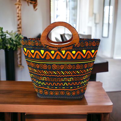 Tote bag with wooden handles features vibrant tribal patterns in orange, yellow, and brown on a black background, conveying a bold and artistic vibe.