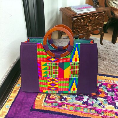 Purple tote bag with vibrant Kente patterns, featuring geometric shapes in red, yellow, green, and blue. Accented with wooden circle handles.