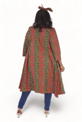 A woman in a vibrant red and green patterned coat with a matching headscarf stands facing away, wearing blue jeans and beige heels, on a white background.