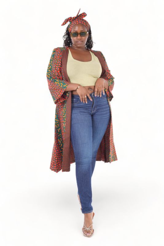Woman in a colorful headwrap and robe, green crop top, and jeans. She wears sunglasses and heels, exuding confidence against a plain background.