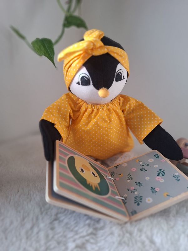 Kleiner handgemachter Stoffpinguin schaut sich ein Buch an.