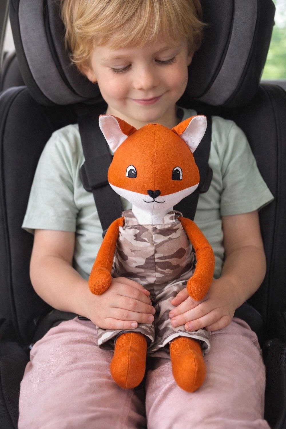 Handgemachtes Stofftier Fuchs sitzt auf dem Schoß eines Kindes im Kindersitz. Hintergrund wurde mit KI generiert.