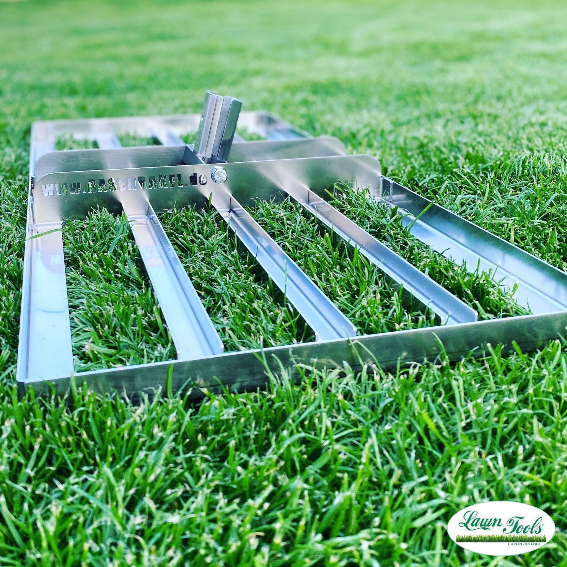„Rasenrakel mit Holzstiel, der auf einem frisch gemähten, grünen Rasen liegt, verwendet für das Nivellieren von Rasenflächen. Im unteren Bereich ist das Logo von Lawn Tools zu sehen.“