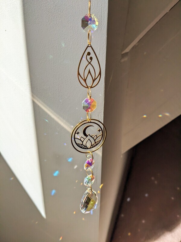 Attrape soleil fait main en pièce unique ou petite série, composé de matériaux durables de qualité. Objet de décoration Feng Shui, l&#39;attrape soleil, invite à l&#39;intérieur de votre maison toutes les belles énergies du soleil en créant un arc-en-ciel lumineux plein de douceur et de magie. Il réharmonise et protège votre intérieur. Fleur de lotus et lune