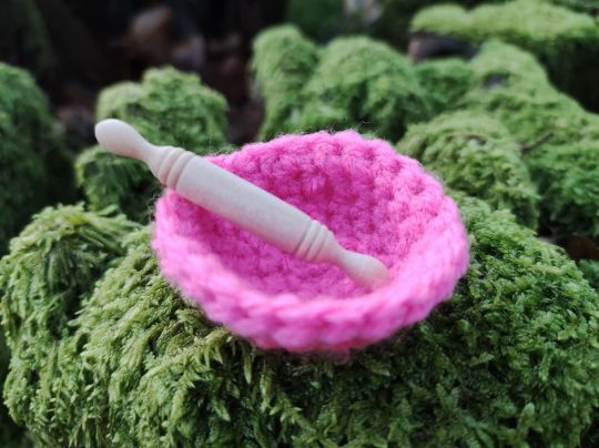 Haekelkorb Pink mit Miniatur Nudelholz aus Holz auf einem bemoosten Hintergrund