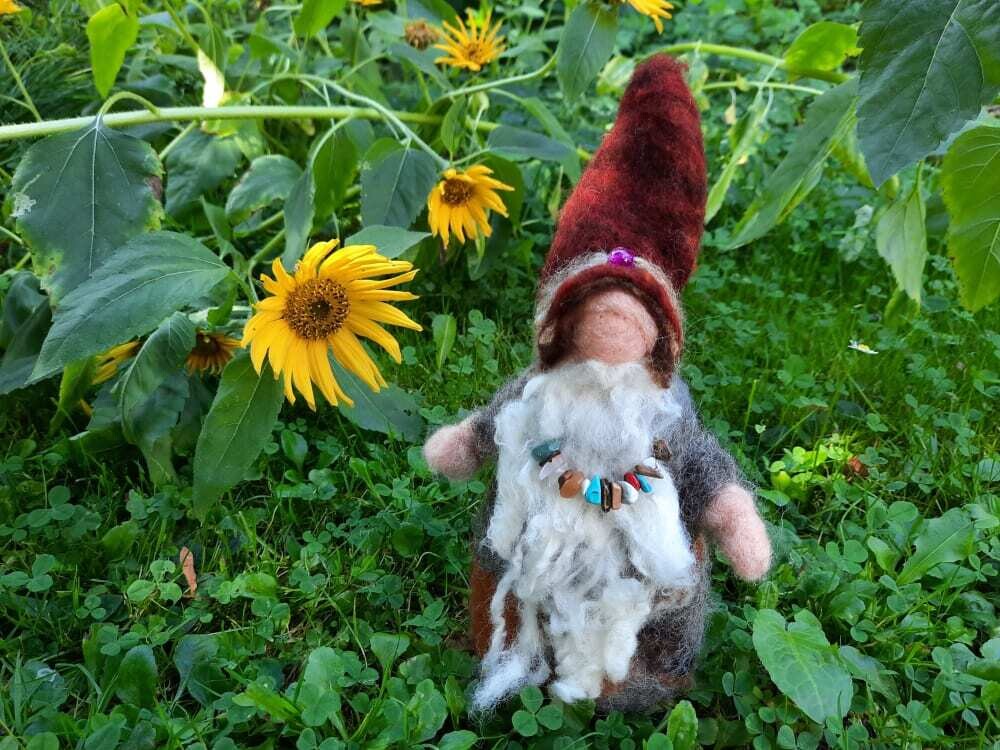 Gefilzter Naturgeist mit weißem Bart und rotbraunem Hut vor Sonnenblumen