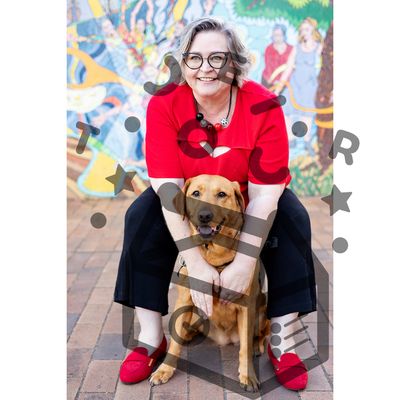 82 Rachael and Helga Caucasian woman sitting and smiling at the camera, wearing a red top. Her service dog sits between her legs.
