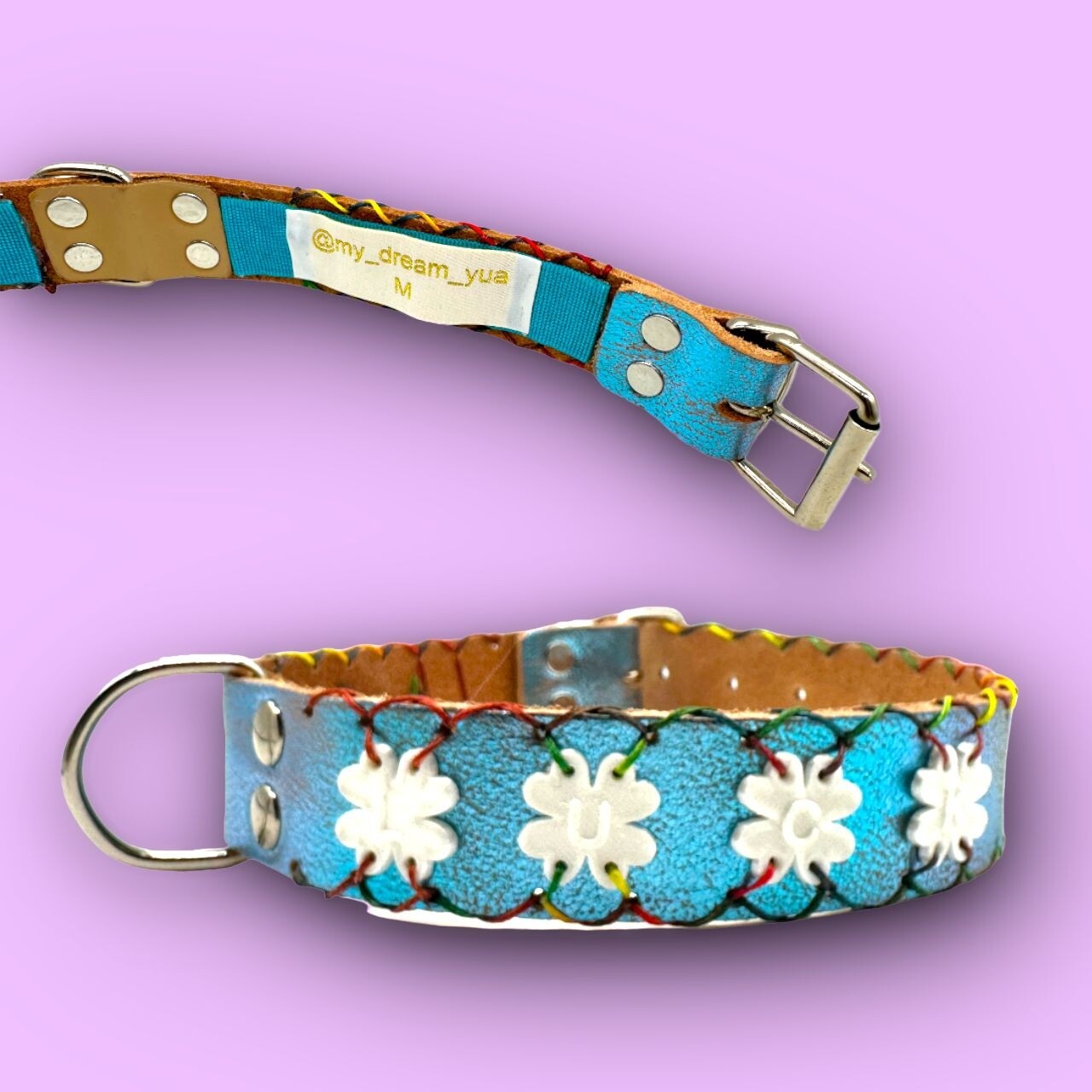 COLLARE in pelle color turchese metallizzato personalizzato con bordatura in contrasto multicolor e charme a forma di quadrifoglio bianchi con scritta LUCK. La taglia del collare è la M. COLLARE in pelle color turchese metallizzato personalizzato con bordatura in contrasto multicolor e charme a forma di quadrifoglio bianchi con scritta LUCK. La taglia del collare è la M.