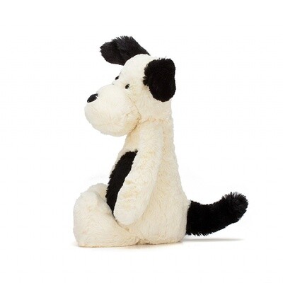 Jellycat Bashful black and cream puppy stuffed animal in medium size, displayed in a cozy lifestyle setting