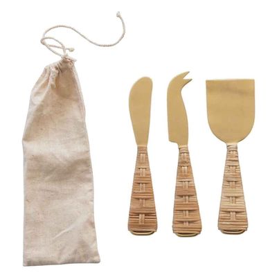 Three gold stainless steel cheese knives with natural rattan-wrapped handles arranged on a white background