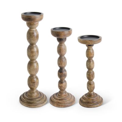 Set of three brown wood spindle candleholders arranged in a row on a neutral background