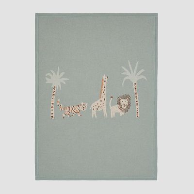 Safari lion jacquard knit baby blanket in cream and tan draped over a wooden chair in a nursery setting