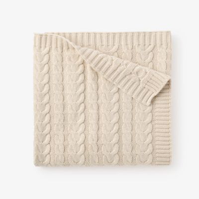 Cream horseshoe cable knit baby blanket draped over a wooden chair in a nursery setting with soft natural light