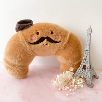 Mon Ami Monsieur Croissant plush toy, a 7-inch French croissant-shaped stuffed animal with soft fabric details in a lifestyle setting