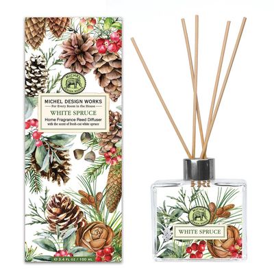 White Spruce reed diffuser by Michel Design Works in a clear glass decanter with rattan reeds on a neutral background