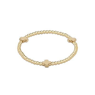 Gold beaded bracelet with small cross charm detail on a neutral background