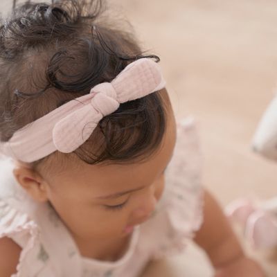 Two organic muslin bow headbands in taupe and blush tones arranged on a soft neutral background