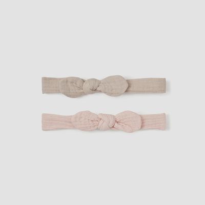 Two organic muslin bow headbands in taupe and blush, displayed side by side on a neutral background