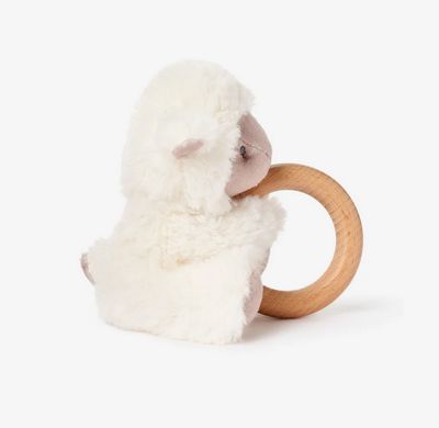 Cream-colored plush lamb toy with wooden ring rattle attachment, displayed in a soft nursery setting.