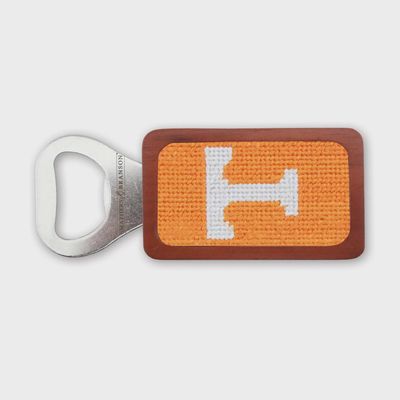 Needlepoint magnetic bottle opener with wood handle displayed in a lifestyle setting, showing the detailed needlepoint design and natural wood grip.