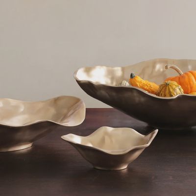 Small oval bowl in champagne gold finish displayed in a lifestyle setting, showcasing the metallic luster and curved form of the serving vessel.