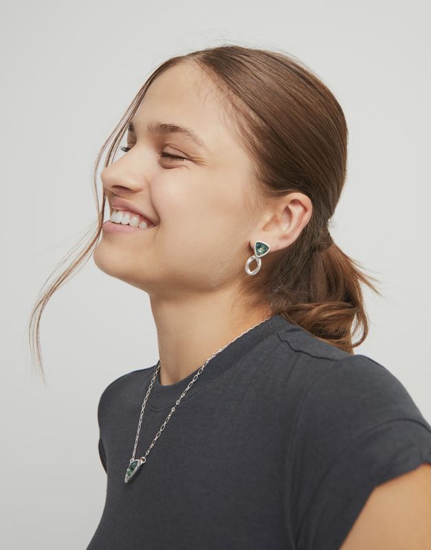 Green crystal stud earrings from Uno de 50 Ser Camaleónica collection worn in a lifestyle setting, showcasing the iridescent green stone detail