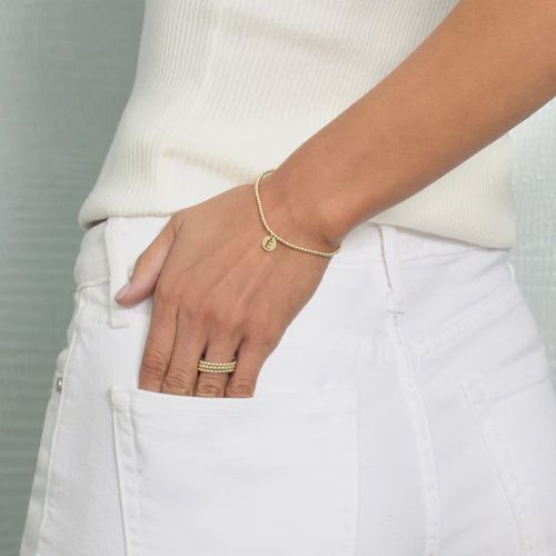 Gold beaded bracelet with personalized initial disc charm worn on a wrist, showcasing the 2mm gold beads and custom engraved letter detail