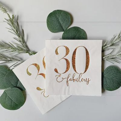 Stack of gold glitter foil cocktail napkins with 30 and Fabulous text on white background