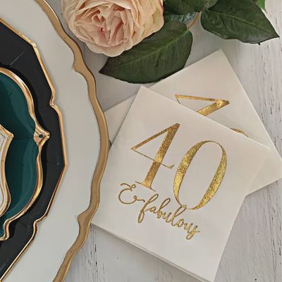 Gold glitter foil cocktail napkins printed with '30 and Fabulous' text arranged on a table setting with drinks and party decorations