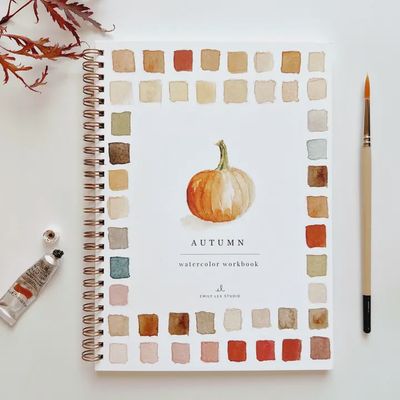 Watercolor Workbook with 12 Step-by-Step Illustrations open on a desk, showing painted pages and instructional content.