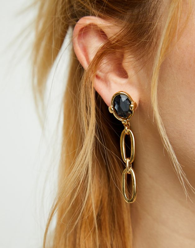 Faceted black crystal link drop earrings with gold-tone hardware worn in a lifestyle setting