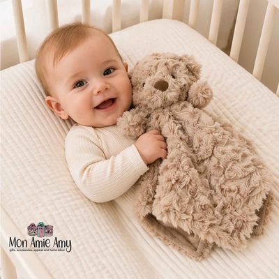Happy baby lying in crib holding a plush teddy bear security blanket lovey for comfort and soothing sleep