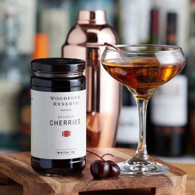 Woodford Reserve bourbon-infused cocktail cherries displayed in a lifestyle setting with a cocktail glass and bar accessories