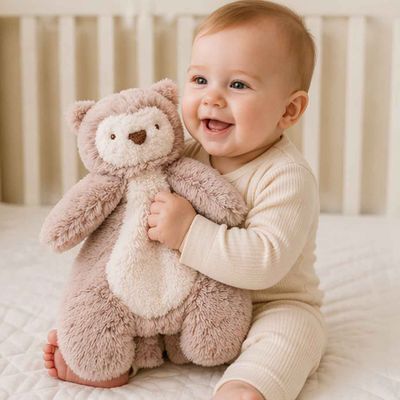Baby in crib holding Olivia the Owl snuggler plush security blanket, cozy baby lovey for comfort and soothing