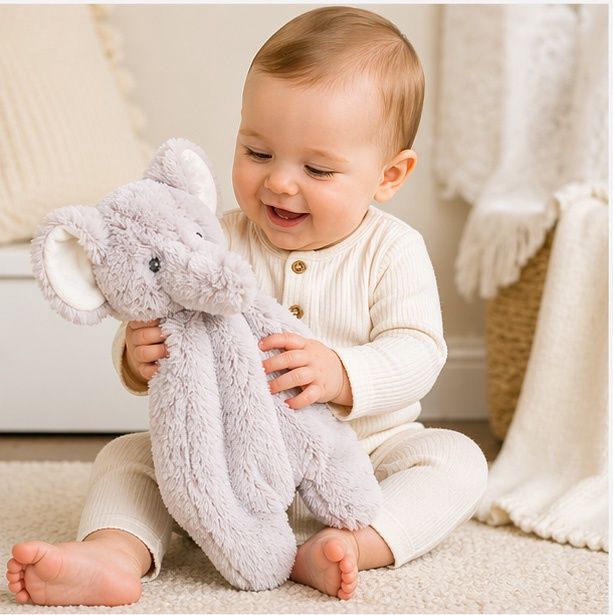 Baby playing with soft elephant snuggler plush lovey toy on carpet in warm neutral nursery setting