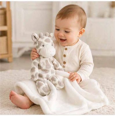 Baby playing with giraffe plush lovey and soft baby blanket on floor in warm neutral nursery setting