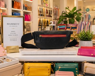 Hammitt Charles Medium black crossbody bag with red zipper and gold hardware displayed in a bright, colorful retail store