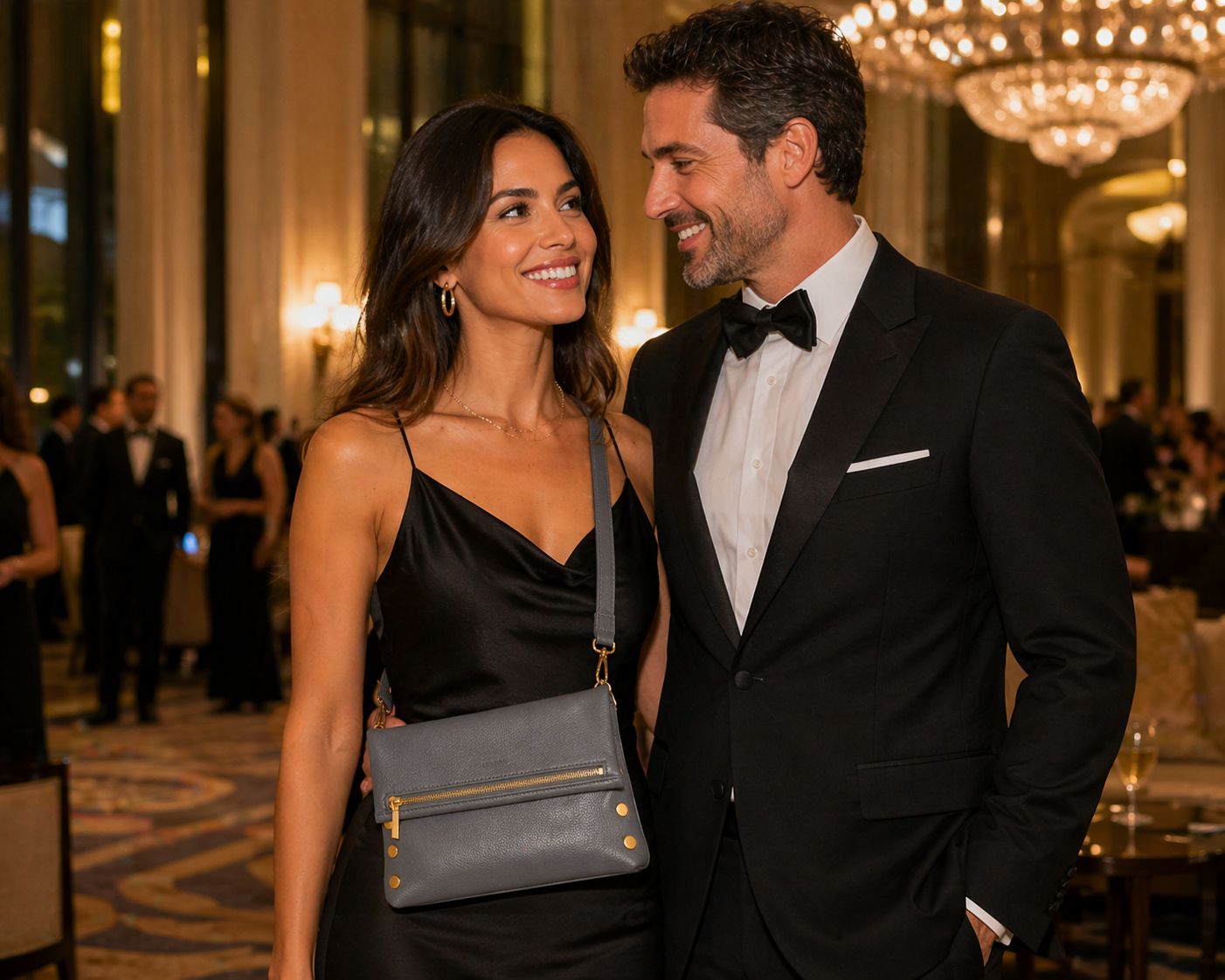 Couple at luxury gala with woman wearing Hammitt VIP Medium Sonnet Grey crossbody bag with brushed gold hardware