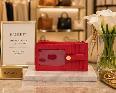 Red leather Hammitt wallet with gold accents showcased on marble display in boutique setting