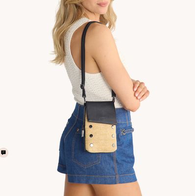 Woman wearing Hammitt VIP Mobile crossbody in chaparral raffia with gunmetal hardware, styled over shoulder with denim skirt