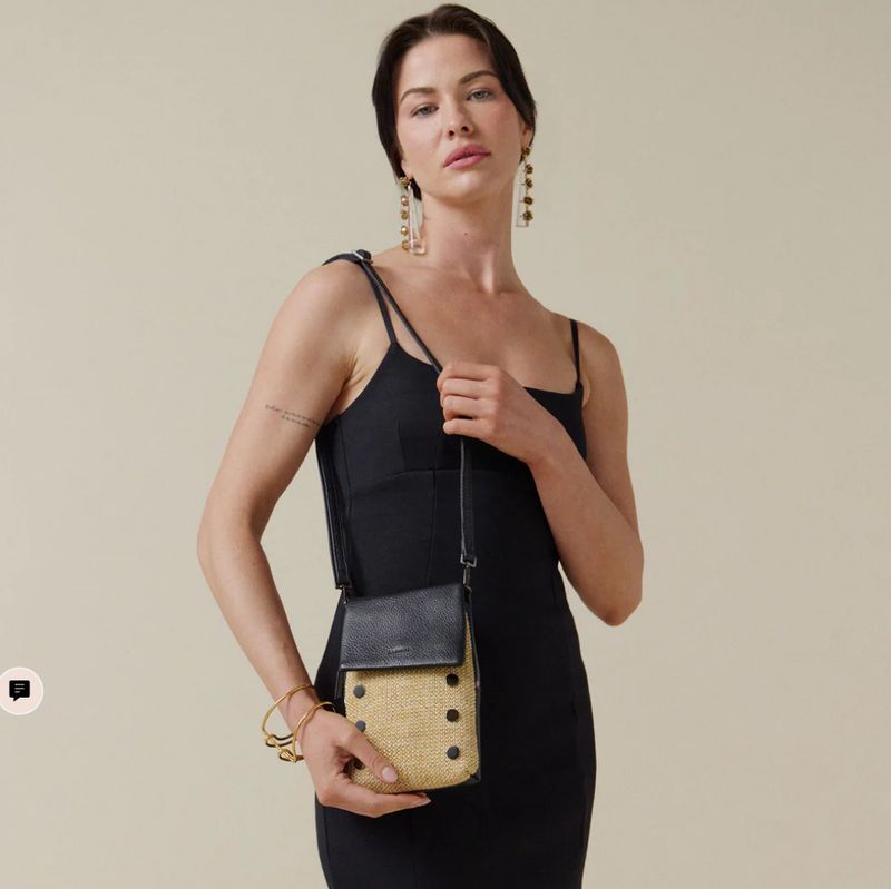 Woman in black dress wearing Hammitt VIP Mobile crossbody in chaparral raffia with gunmetal hardware, styled as a chic phone 