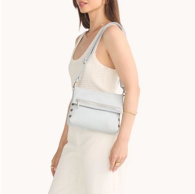 Woman in a neutral outfit holding a Hammitt VIP Med Bluebird clutch, styled with wide-leg pants and a sleeveless top on a cle