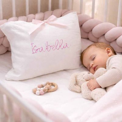 Sleeping baby girl in crib with personalized pillow featuring pink embroidered name Isabella