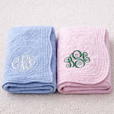 Folded pink and blue baby quilts with embroidered monograms, soft personalized infant blankets displayed side by side