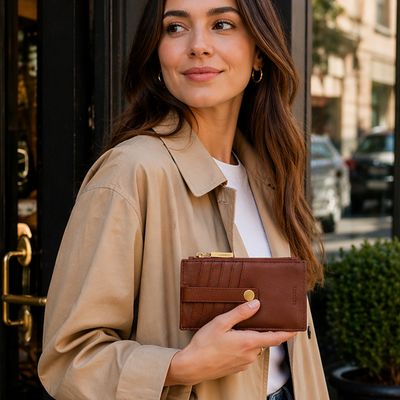 Woman holding Hammitt 210 West Small chocolate pebble leather wallet outdoors, stylish everyday carry accessory