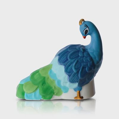 Hand-painted peacock mini tabletop piece by Nora Fleming with detailed feather work and vibrant colors on a neutral background