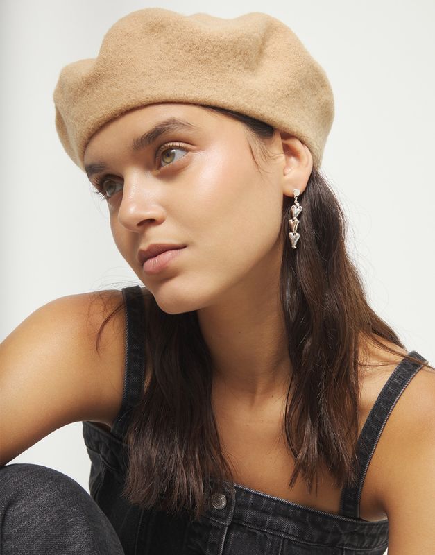 Uno de 50 Chained Hearts Drop Earrings in gold-tone metal with linked heart charms dangling from chain, worn in a lifestyle setting.