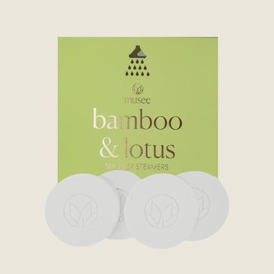 Musee Bamboo &amp; Lotus shower steamers displayed in studio setting against white background, showcasing round tablet forms in green and cream tones.