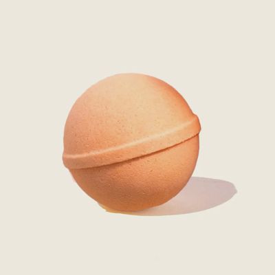 Musee Peach Dream Bath Balm displayed in a lifestyle setting, showing the peachy-pink sphere with a surprise keychain nestled inside.