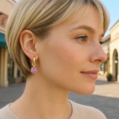 Gold huggie hoop earrings with small reflection charm and February birthstone detail displayed in a lifestyle setting